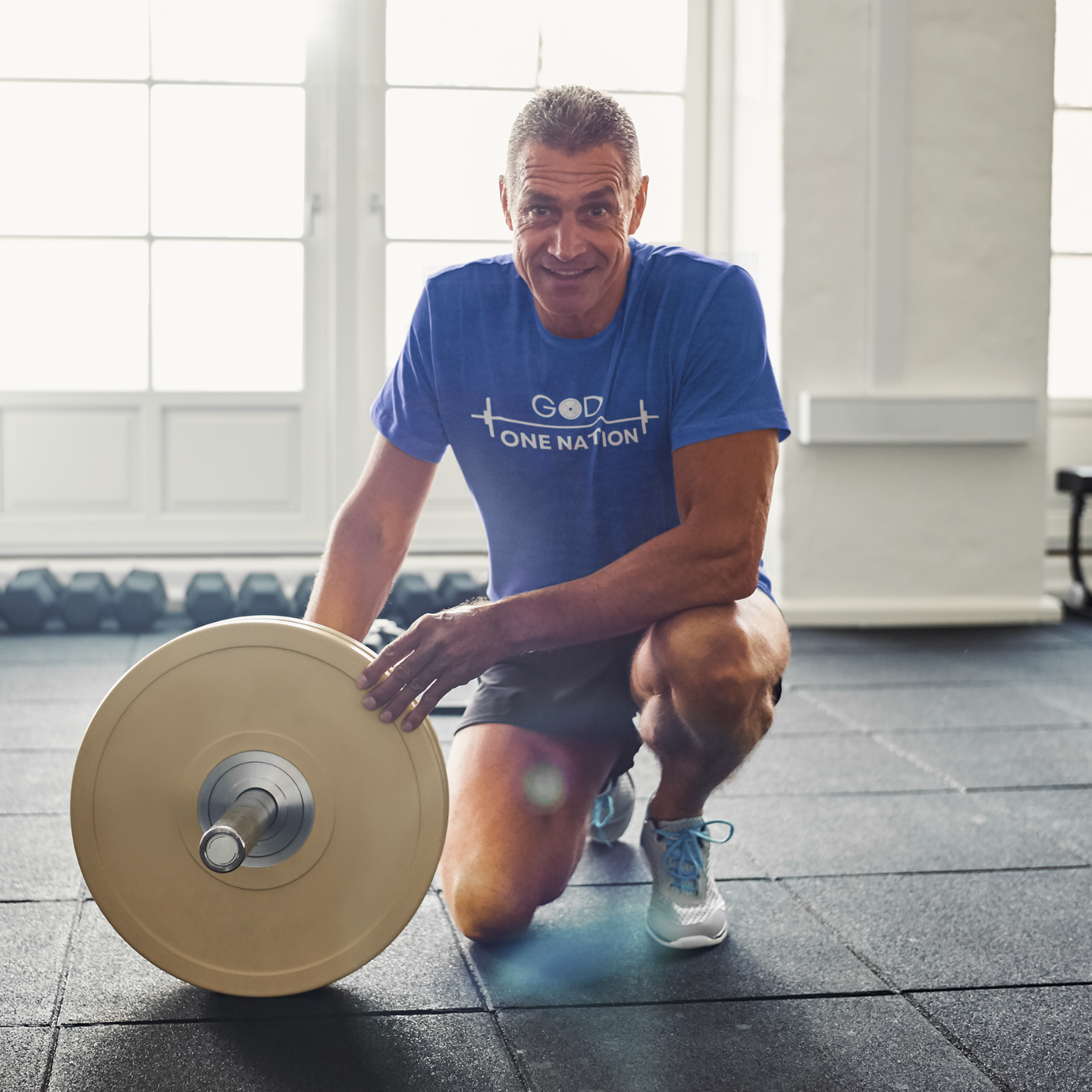 God one nation motivational workout shirt featured by a fit man with weights around at the gym