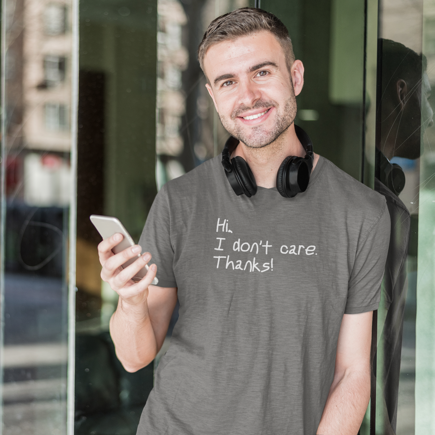 Gym-t-shirt-Hi-I-Don_t-Care-Thanks-on-a-man-posing-with-headphones-around-his-neck-and-holding-a-smartphone