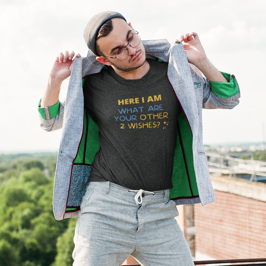 Funny gym shirt with text Hear I Am, What Are Your Other 2 Wishes?, the graphic workout shirt is in dark grey heather almost black color and is worn by a middle age man showing it in a park