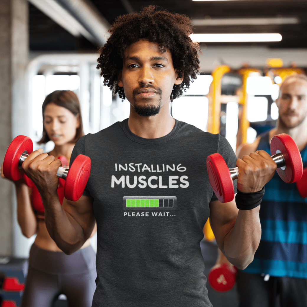 Funny gym shirt with text installing muscles please wait worn by a man lifting dumbbells