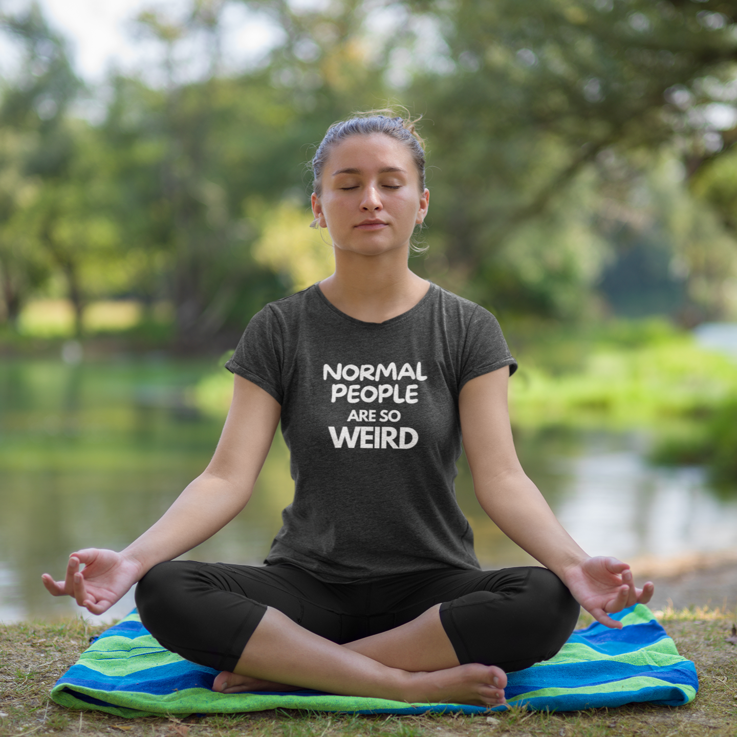 Funny gym shirt with text people are so weird in dark heather grey almost black color worn by a young woman doing yoga in the park