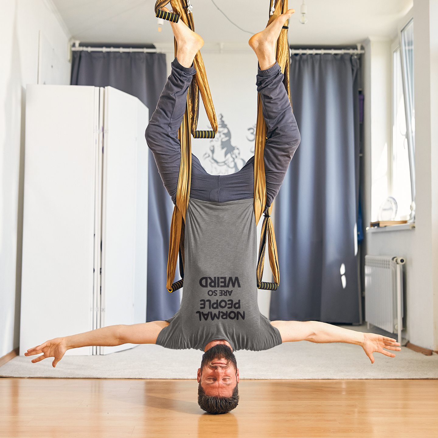 Funny workout shirt with text people are so weird worn by a man hanging upside down from aerial yoga silk
