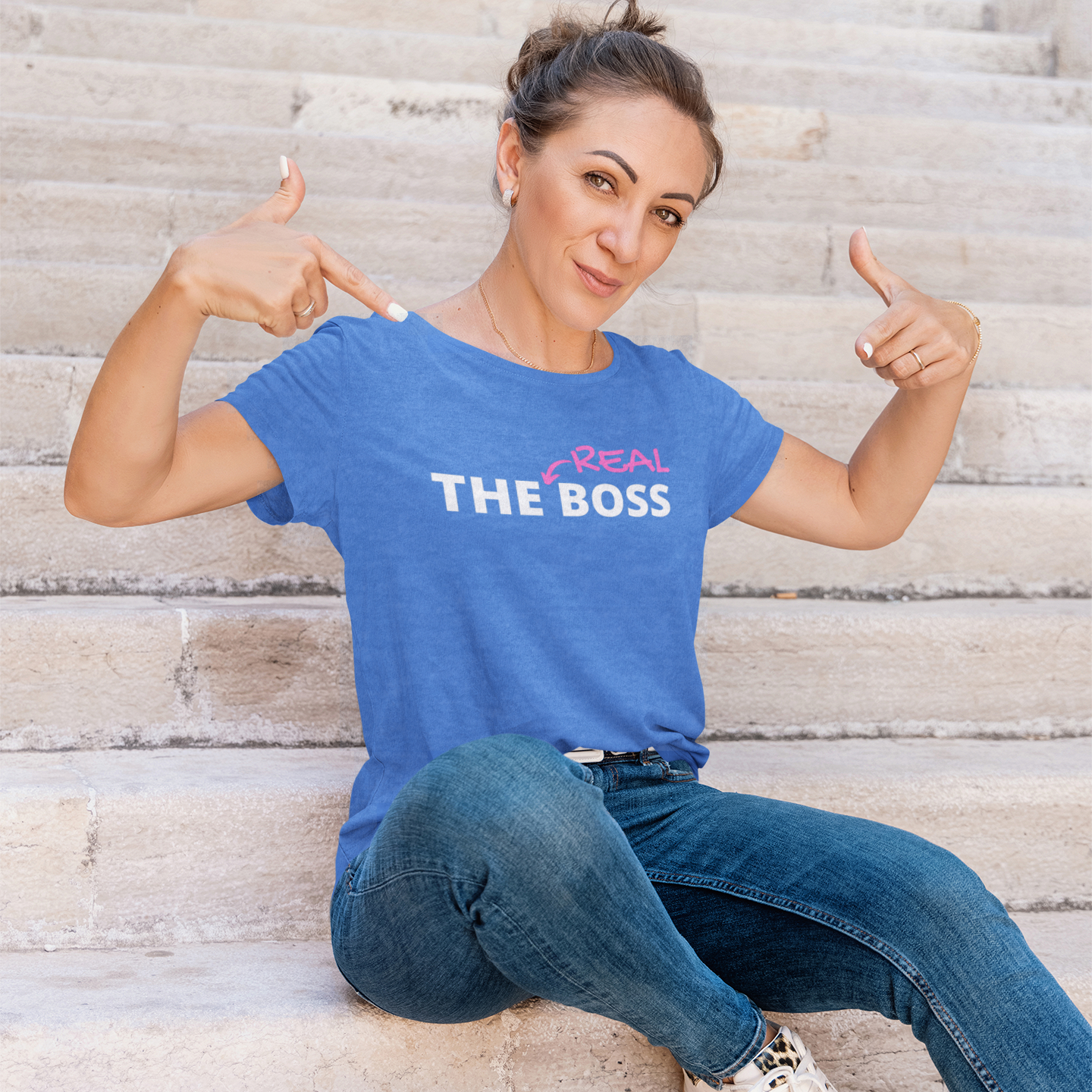Sarcastic-T-shirt-with-The-Real-Boss-text-by-a-woman-pointing-at-the-text-while-posing-by-the-stairs
