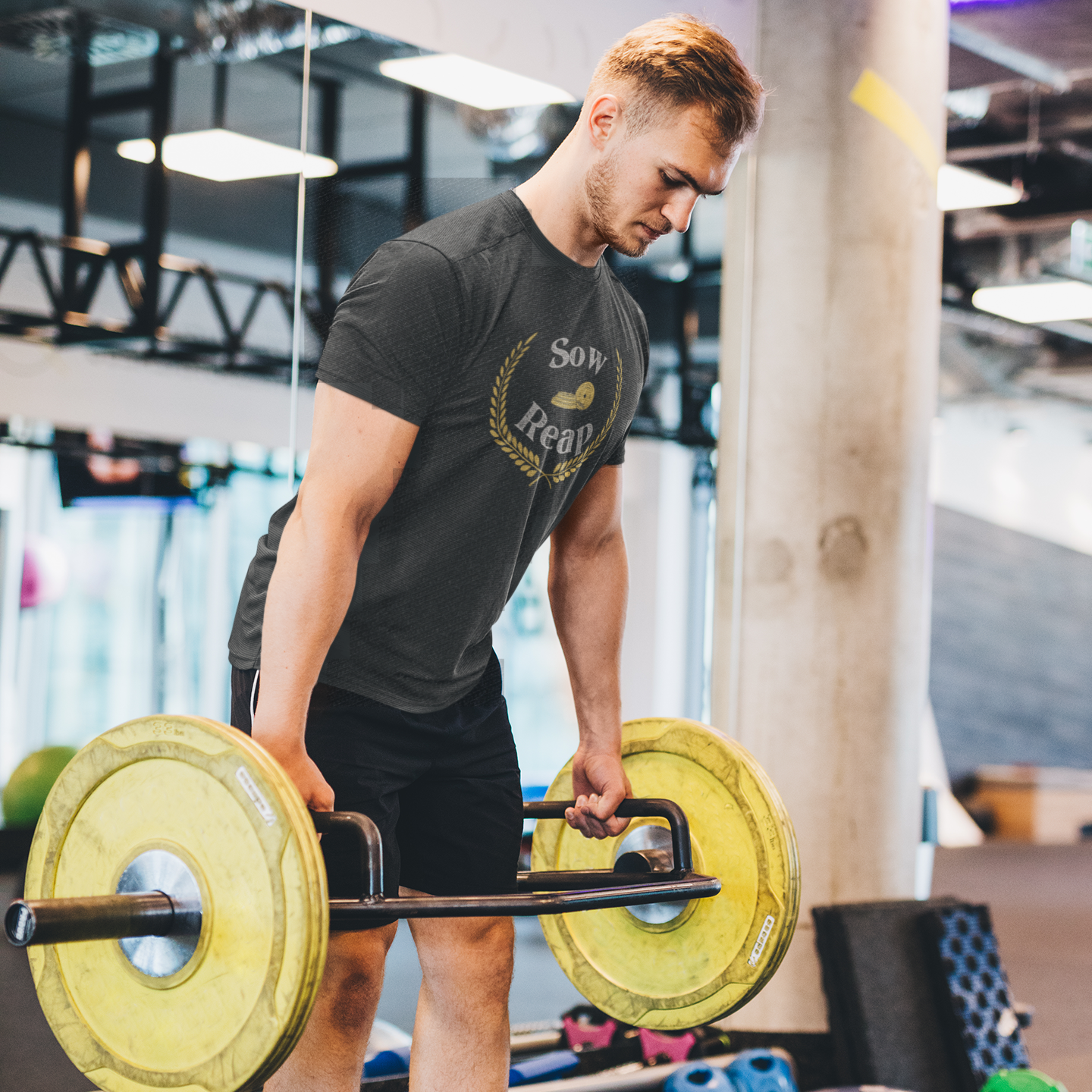 Motivational workout shirt with words Sow and Reap and with gym plates with victory laurel wreath worn by man doing deadlift at the gym